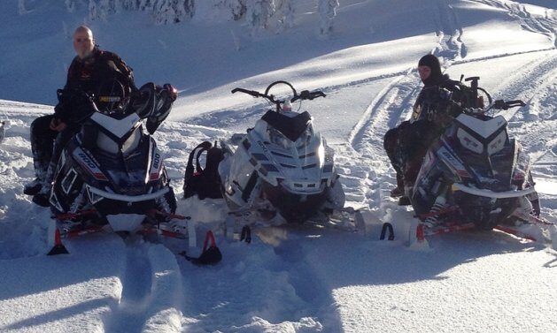 Three snowmobilers resting on their sleds in deep snow near Sicamous